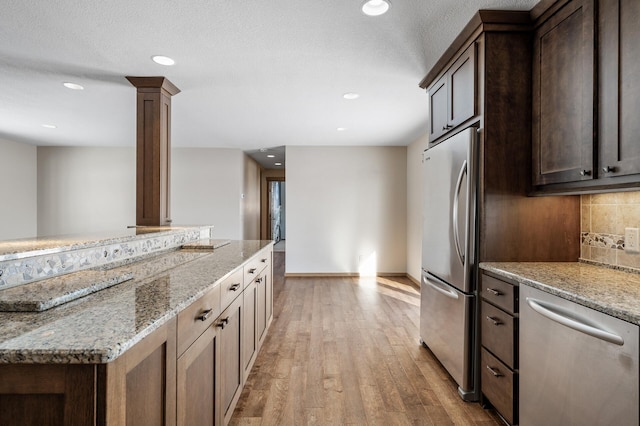 kitchen with light wood-style flooring, light stone countertops, stainless steel appliances, decorative backsplash, and decorative columns