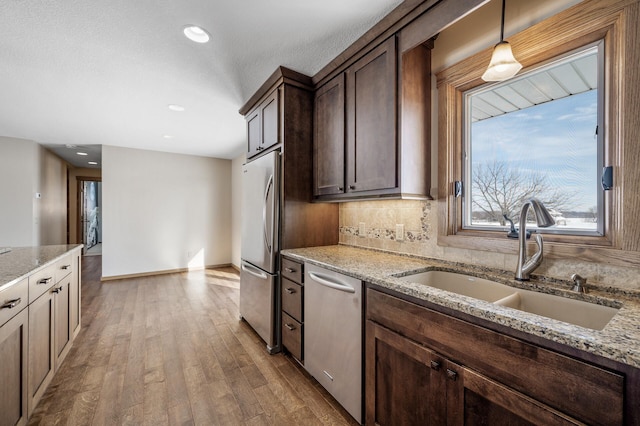 kitchen featuring wood finished floors, a sink, hanging light fixtures, appliances with stainless steel finishes, and light stone countertops