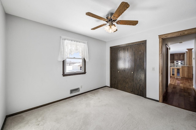 unfurnished bedroom featuring light carpet, ceiling fan, a closet, and baseboards