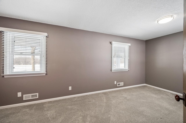 spare room with baseboards, visible vents, a textured ceiling, and light colored carpet