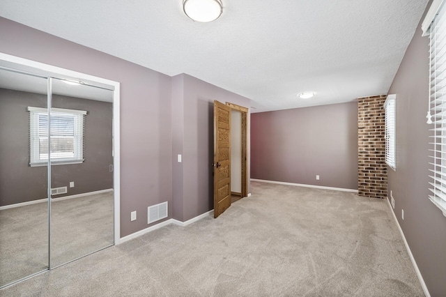 unfurnished bedroom featuring a closet, visible vents, light carpet, a textured ceiling, and baseboards