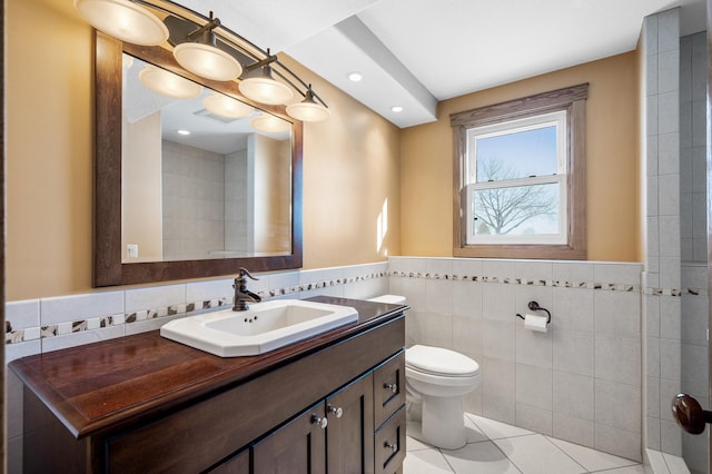 bathroom with toilet, a wainscoted wall, tile patterned floors, vanity, and tile walls