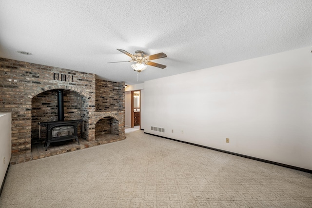 unfurnished living room featuring a wood stove, a ceiling fan, visible vents, and a textured ceiling