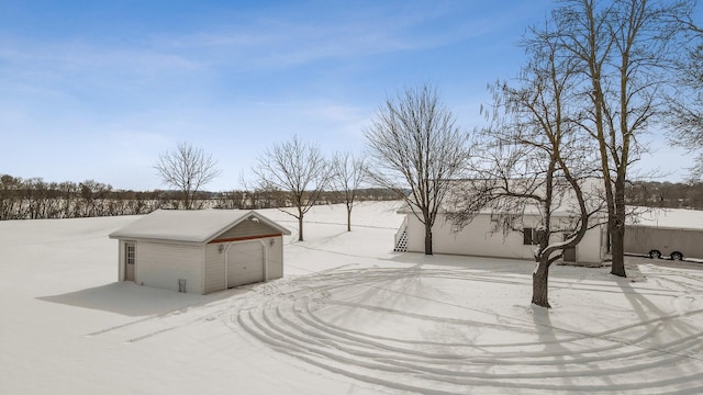 snowy yard featuring an outbuilding, a detached garage, and stairs