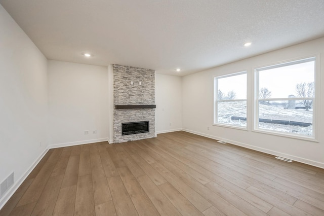 unfurnished living room featuring a fireplace, light hardwood / wood-style floors, and a textured ceiling