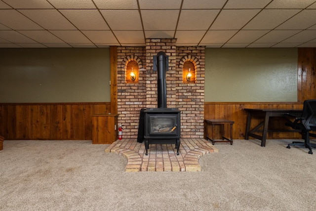 living room featuring a paneled ceiling, wooden walls, carpet, and a wood stove