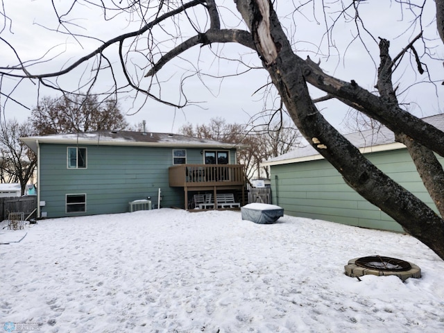 snow covered back of property with a deck and a fire pit