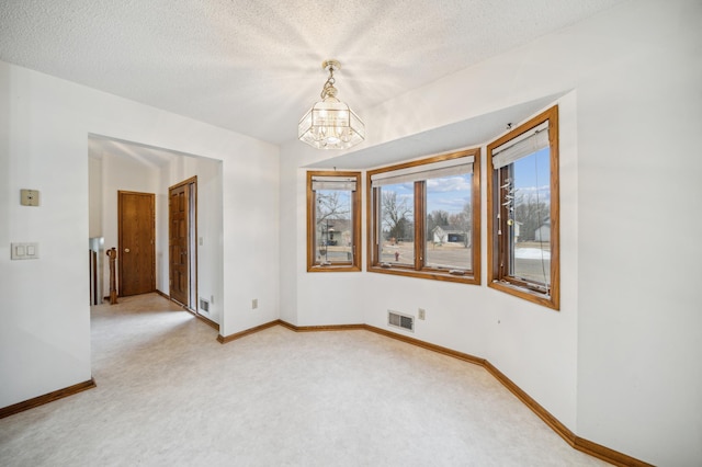 carpeted spare room with a notable chandelier and a textured ceiling