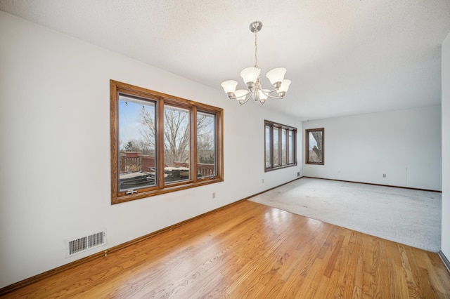 empty room featuring an inviting chandelier, light hardwood / wood-style floors, and a textured ceiling