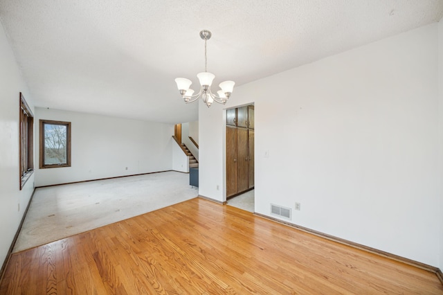 empty room featuring a chandelier, light hardwood / wood-style flooring, and a textured ceiling