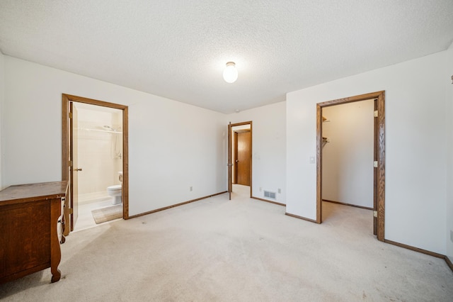 unfurnished bedroom featuring ensuite bath, a spacious closet, light carpet, and a textured ceiling