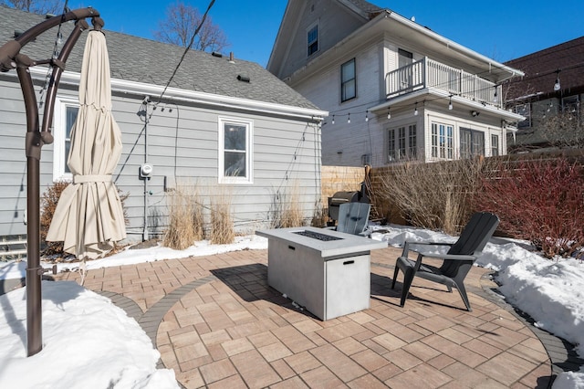 snow covered patio featuring fence, a fire pit, and a balcony