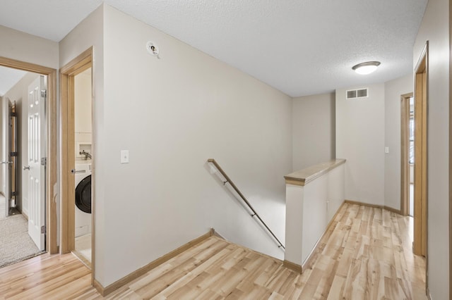 hall featuring washer / clothes dryer, a textured ceiling, and light wood-type flooring