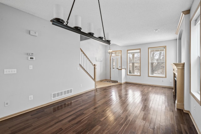 unfurnished living room featuring dark hardwood / wood-style floors, a textured ceiling, and a notable chandelier