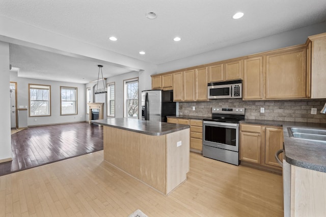 kitchen with a kitchen island, appliances with stainless steel finishes, backsplash, hanging light fixtures, and light hardwood / wood-style floors