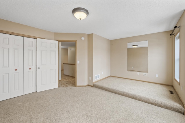 unfurnished bedroom featuring multiple windows, light colored carpet, and a textured ceiling