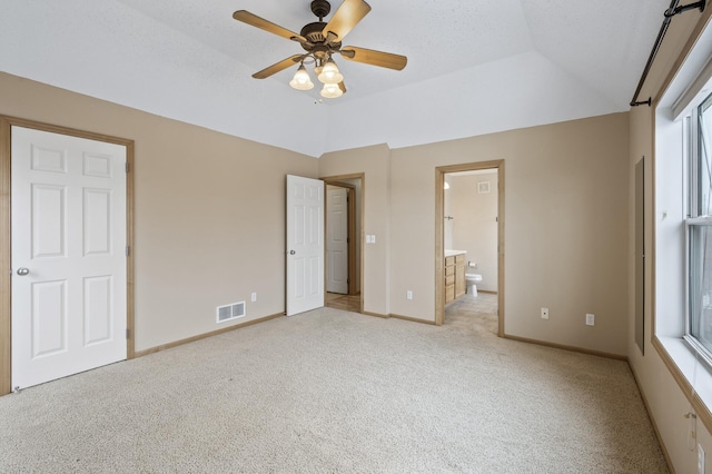 unfurnished bedroom with ensuite bath, vaulted ceiling, light carpet, and a textured ceiling