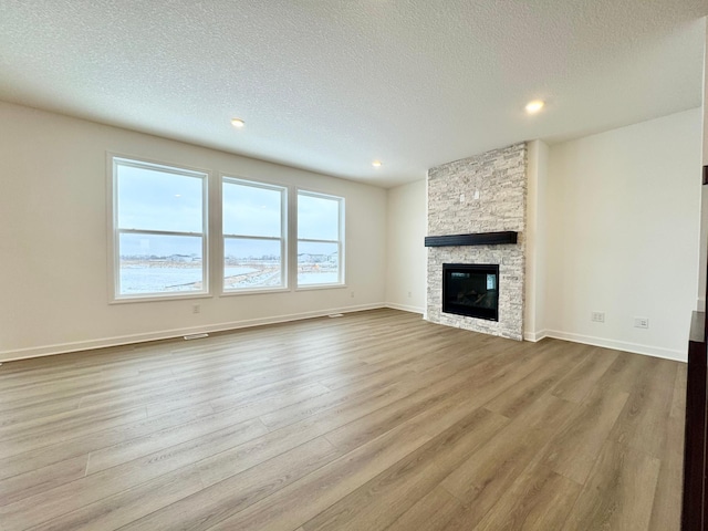 unfurnished living room with a stone fireplace, light hardwood / wood-style flooring, and a textured ceiling