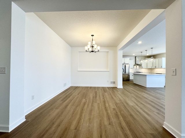 unfurnished dining area with a notable chandelier, wood-type flooring, and a textured ceiling