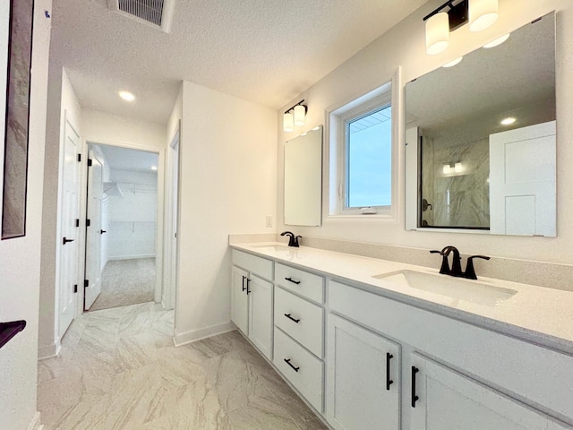 bathroom with vanity, tiled shower, and a textured ceiling