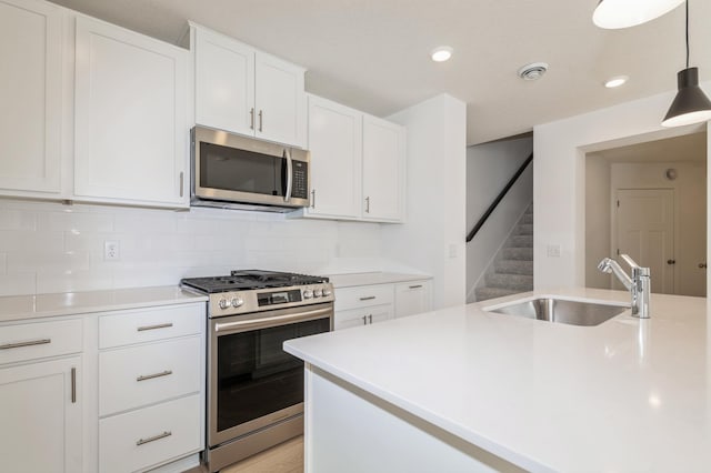 kitchen with sink, white cabinetry, tasteful backsplash, hanging light fixtures, and stainless steel appliances