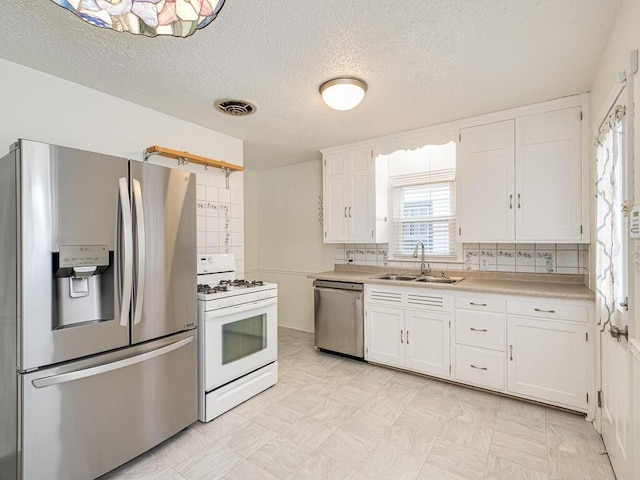 kitchen with sink, white cabinetry, a textured ceiling, appliances with stainless steel finishes, and backsplash