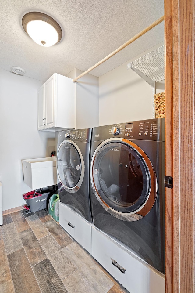 clothes washing area with cabinet space, a textured ceiling, and independent washer and dryer