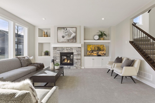 carpeted living room with built in shelves and a stone fireplace