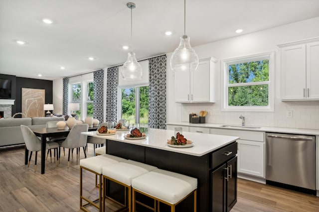 kitchen featuring white cabinetry, sink, stainless steel dishwasher, and hanging light fixtures