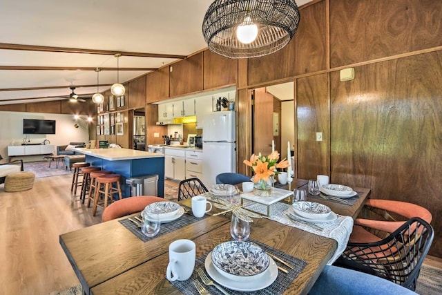 dining room with lofted ceiling with beams, light hardwood / wood-style floors, wooden walls, and ceiling fan