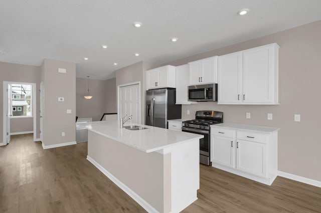 kitchen with stainless steel appliances, a kitchen island with sink, white cabinetry, wood finished floors, and baseboards