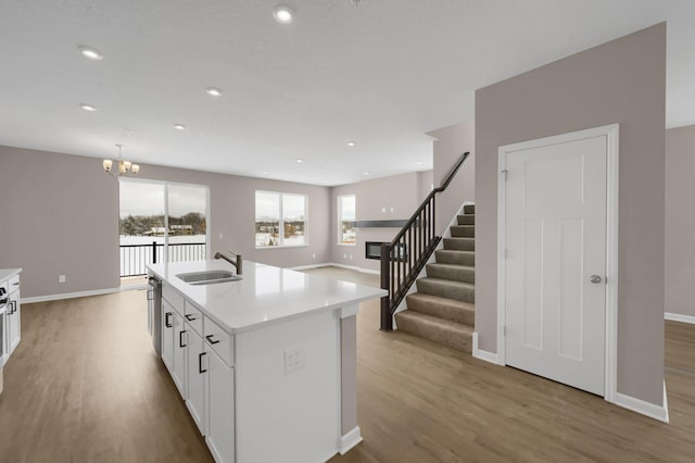 kitchen featuring a center island with sink, white cabinets, light countertops, light wood-type flooring, and a sink