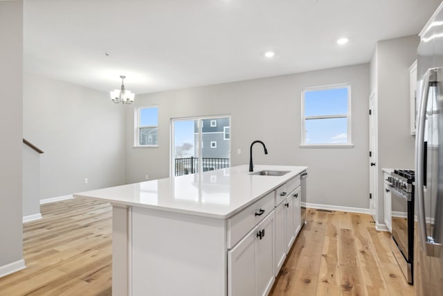 kitchen with pendant lighting, sink, appliances with stainless steel finishes, a kitchen island with sink, and white cabinetry