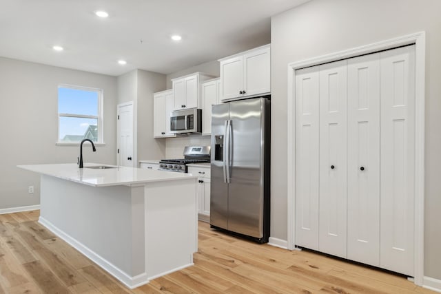 kitchen with appliances with stainless steel finishes, a kitchen island with sink, light countertops, white cabinetry, and a sink