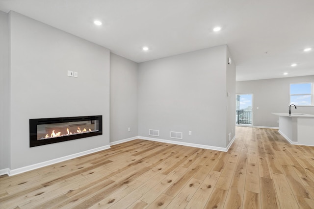 unfurnished living room with light wood-type flooring, visible vents, a glass covered fireplace, and recessed lighting