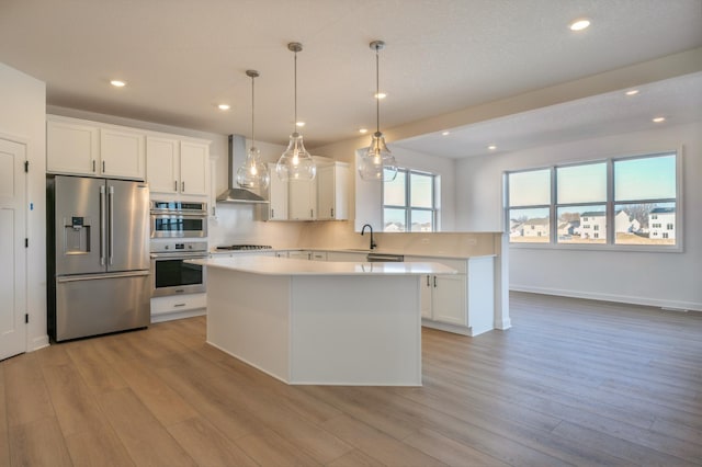 kitchen with white cabinets, hanging light fixtures, a center island, stainless steel appliances, and wall chimney range hood