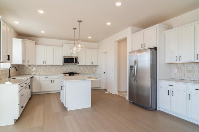 kitchen featuring a kitchen island, appliances with stainless steel finishes, decorative light fixtures, white cabinetry, and sink