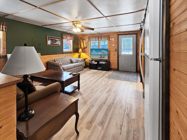 living room with ceiling fan, light wood-type flooring, and wooden walls