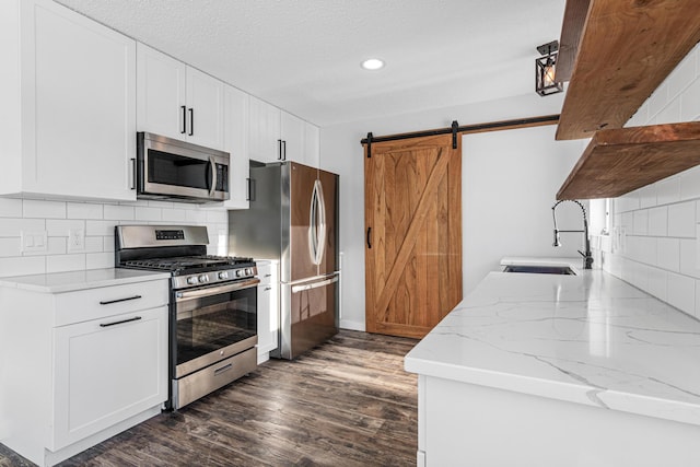 kitchen with dark wood-style floors, tasteful backsplash, a barn door, appliances with stainless steel finishes, and a sink