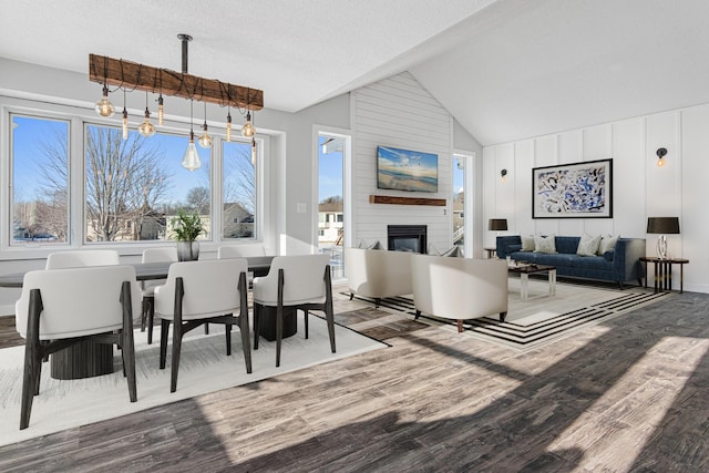 dining area featuring a textured ceiling, a fireplace, vaulted ceiling, and wood finished floors