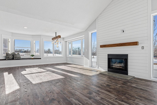 unfurnished living room featuring a large fireplace, baseboards, lofted ceiling, wood finished floors, and an inviting chandelier