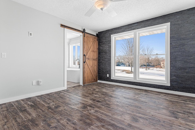 unfurnished room with wood finished floors, a textured ceiling, baseboards, and a barn door