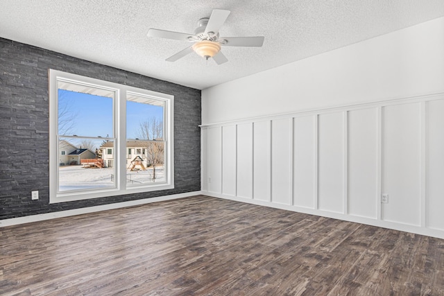 interior space featuring a textured ceiling, ceiling fan, dark wood-style flooring, and a decorative wall