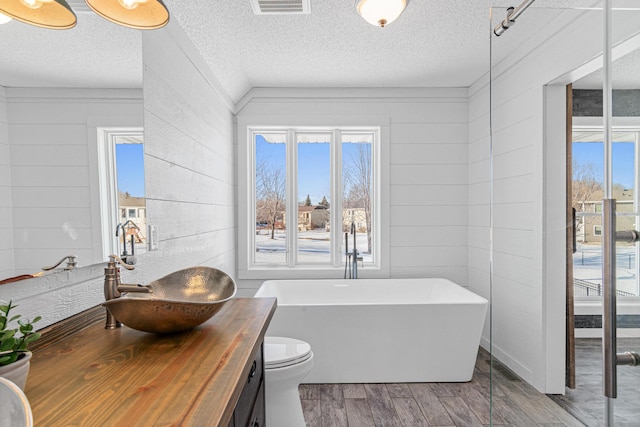 bathroom with visible vents, wood finished floors, a textured ceiling, vanity, and a freestanding tub