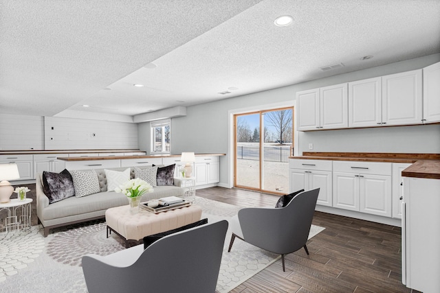 living room featuring a textured ceiling, dark wood-type flooring, visible vents, and recessed lighting