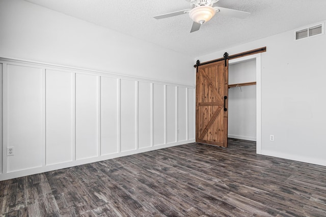 unfurnished bedroom featuring a barn door, a textured ceiling, visible vents, and dark wood-type flooring