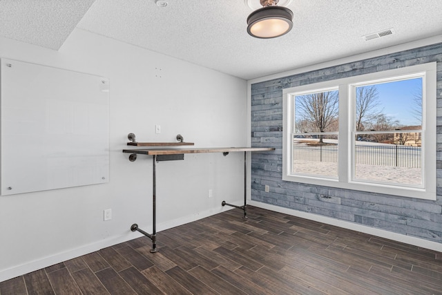 interior space featuring visible vents, a textured ceiling, baseboards, and wood finished floors