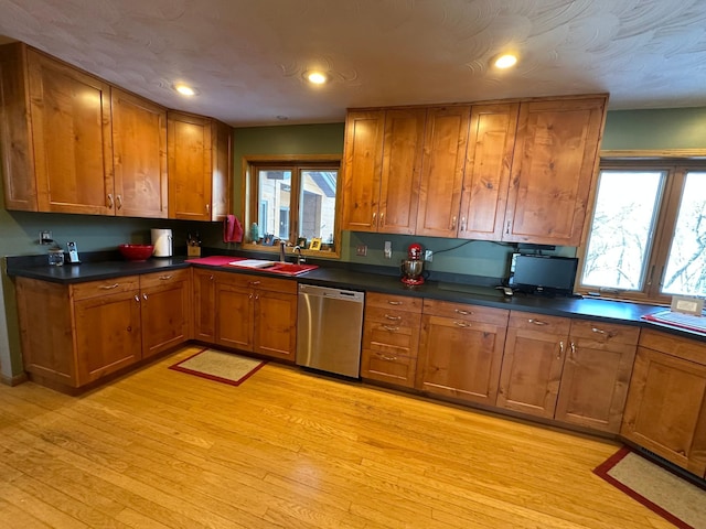 kitchen with brown cabinetry, stainless steel dishwasher, a sink, and a wealth of natural light