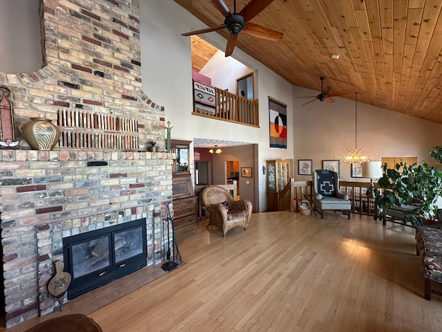 living room with high vaulted ceiling, ceiling fan with notable chandelier, hardwood / wood-style flooring, a glass covered fireplace, and wooden ceiling