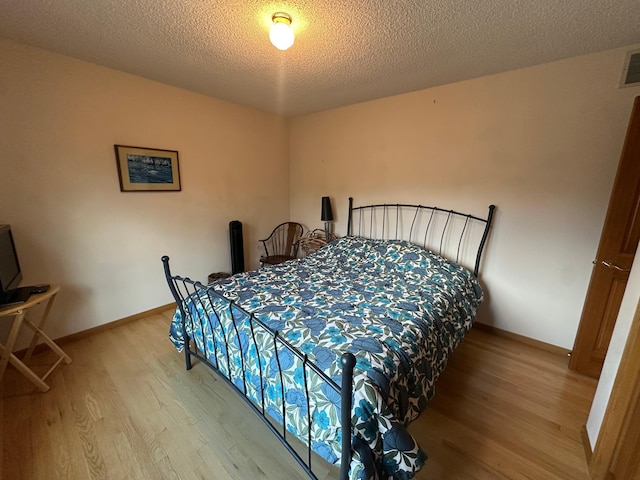 bedroom with a textured ceiling, light wood finished floors, and baseboards